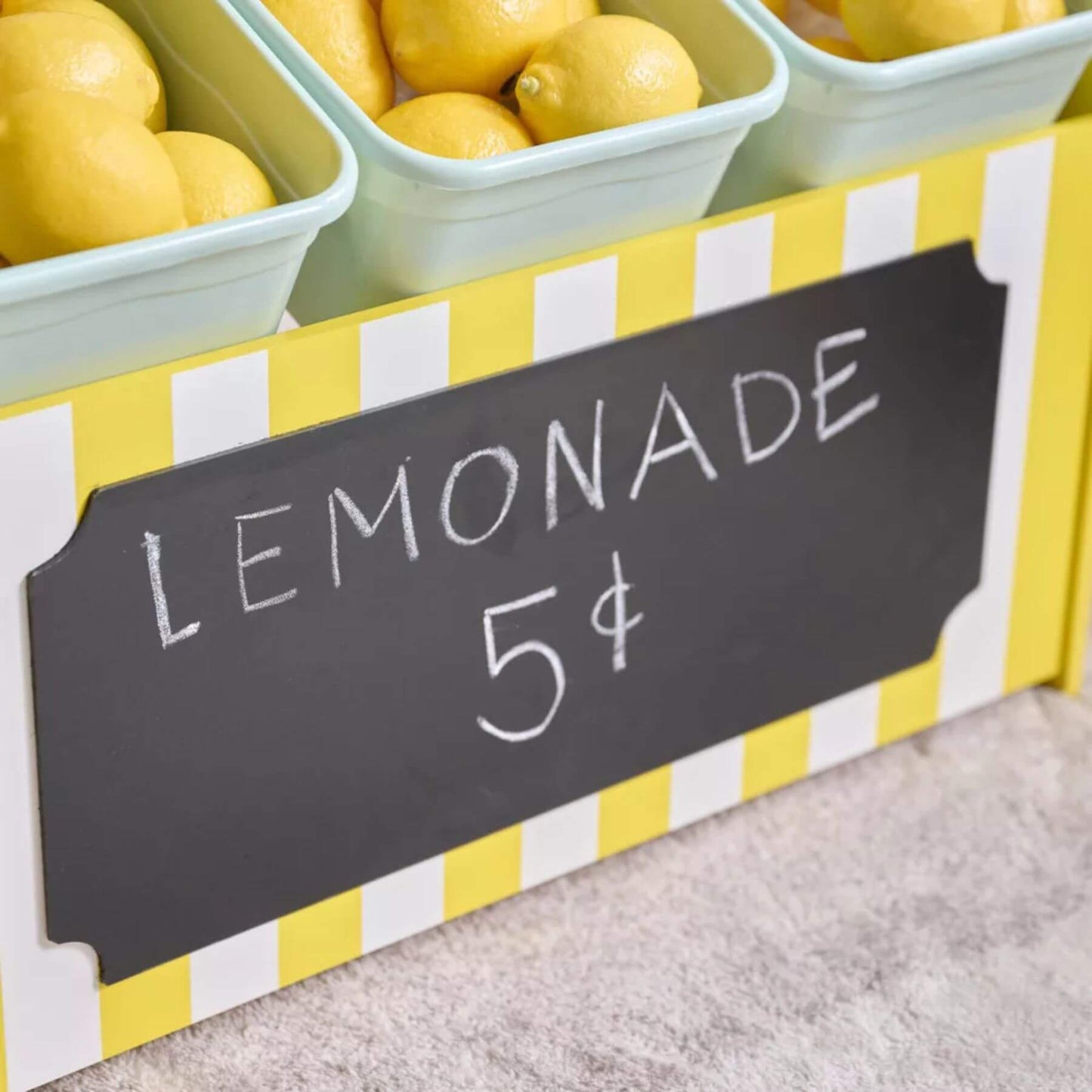Containers of lemons with a lemonade stand sign on a striped stand.
