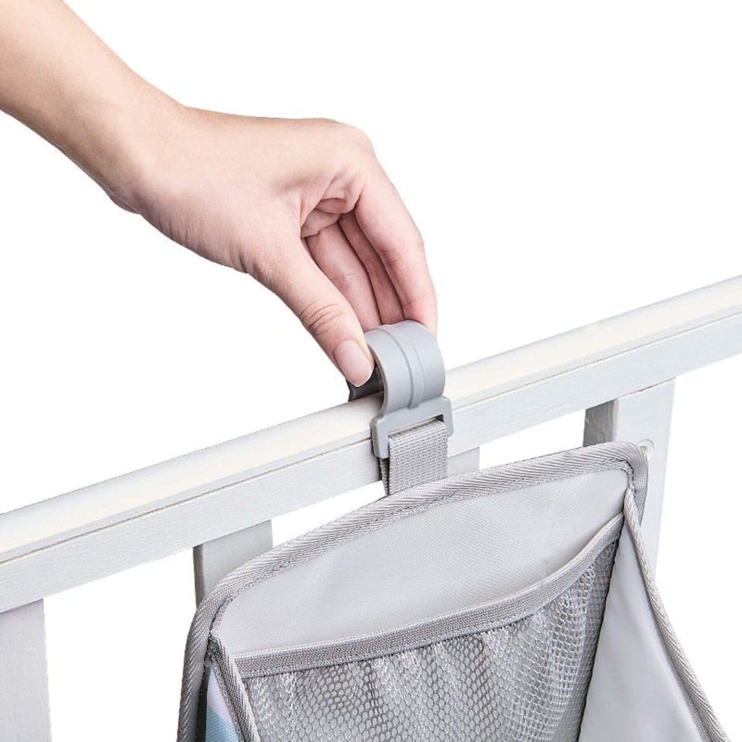 Hand holding a gray mesh organizer attached to a white crib rail.
