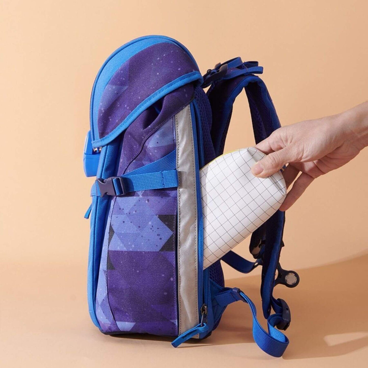 Sunveno Over-clip Kids School Backpack Blue being held open by a hand against a beige background