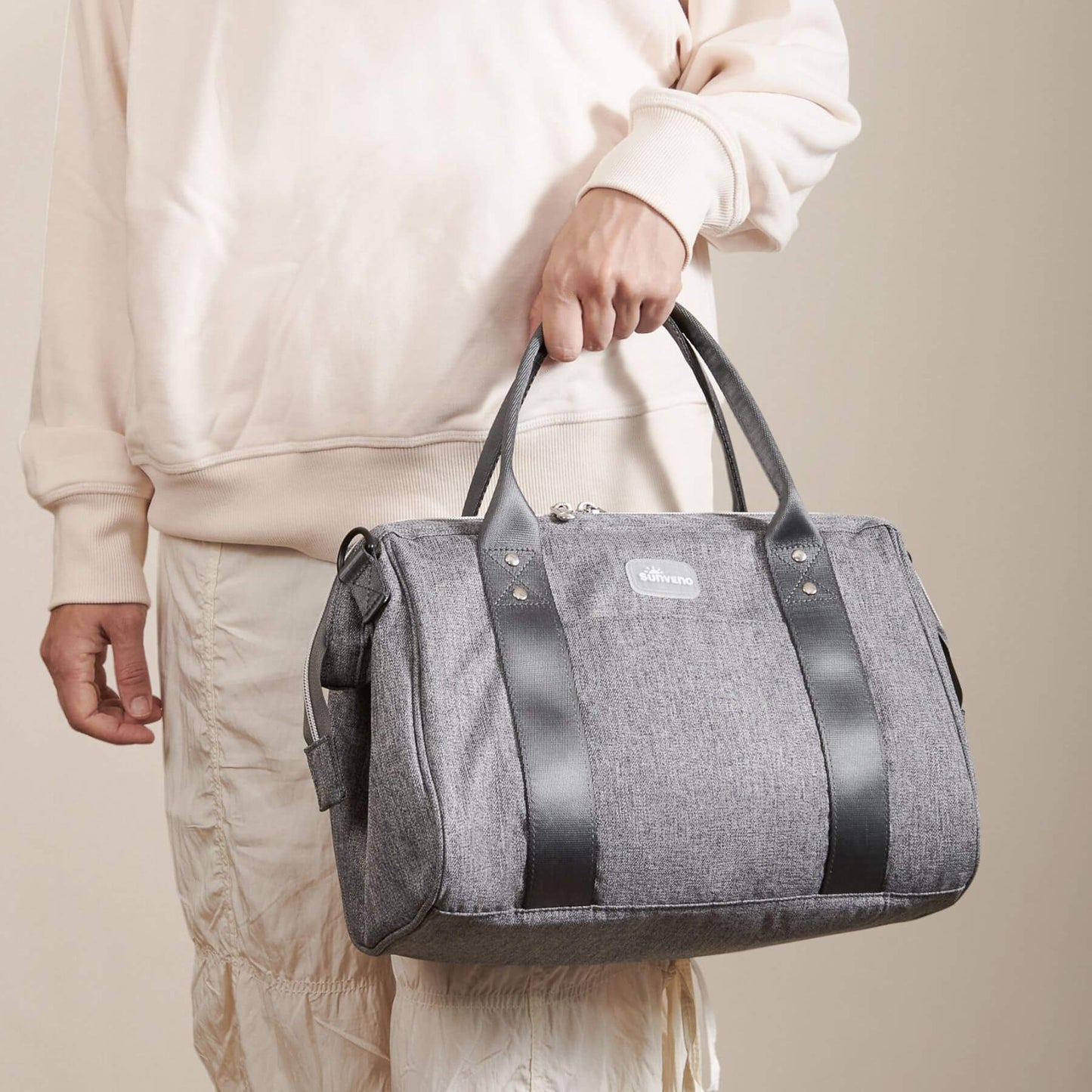 Person holding Sunveno Small Crossbody Diaper Bag against a beige background