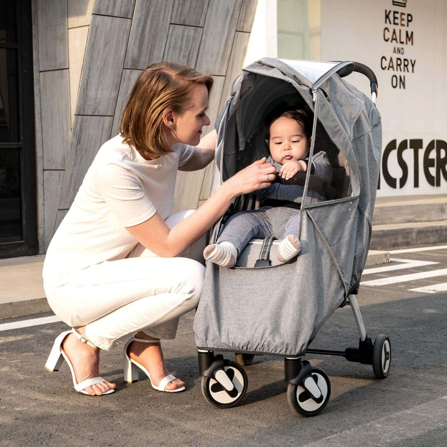 Woman buckling a baby on stroller covered by Sunveno Universal Stroller Cover Gray
