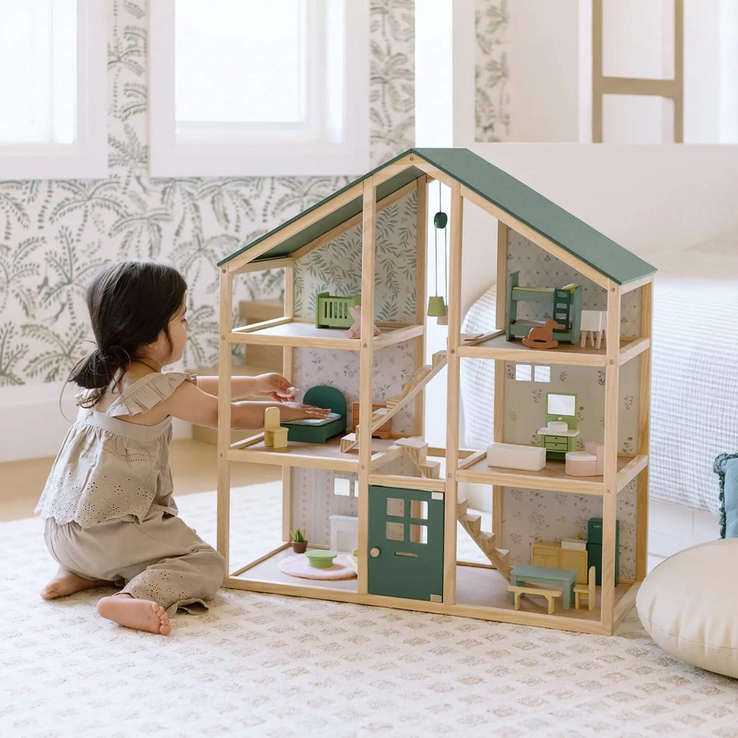 Child playing with Sweetwood Evergreen Dollhouse in a room with light-colored walls and a rug.