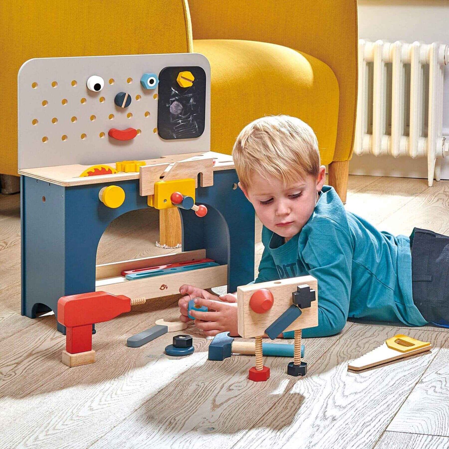 Child playing with Tender Leaf Table Top Tool Bench in a room with a yellow chair.