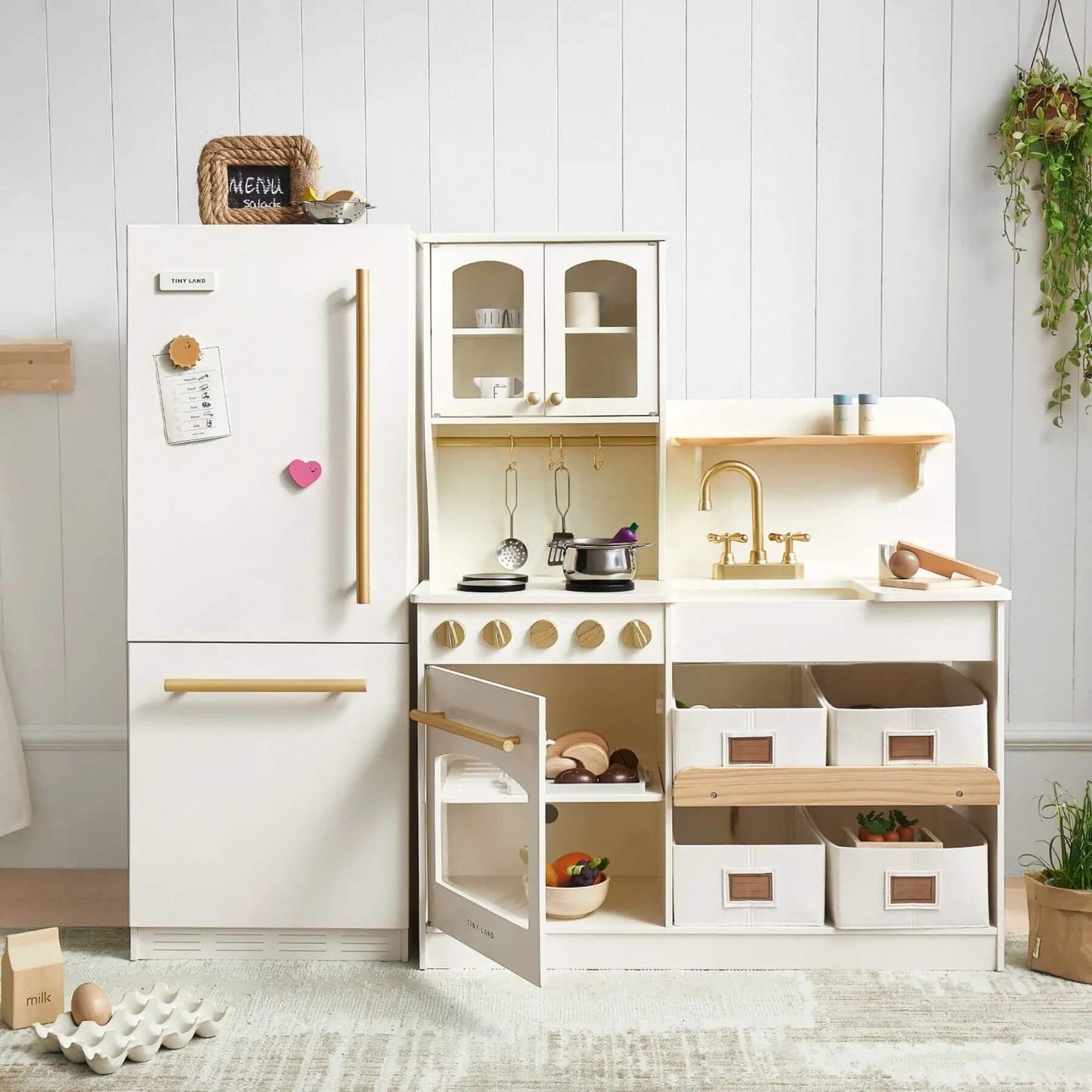 Children's play kitchen set with white cabinets and wooden accents in a room setting.