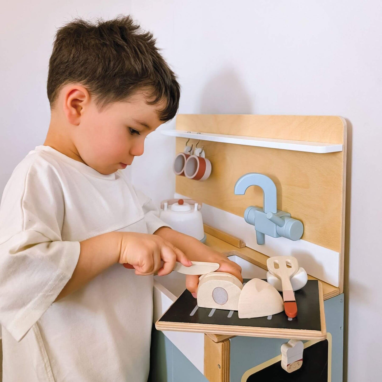 Child playing with Tender Leaf Home Kitchen against a white wall.