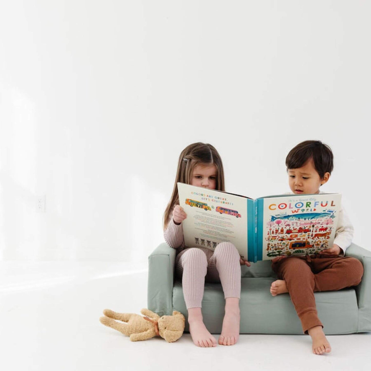 Two children sitting on Toki Kids Sage Play Couch reading a book together.