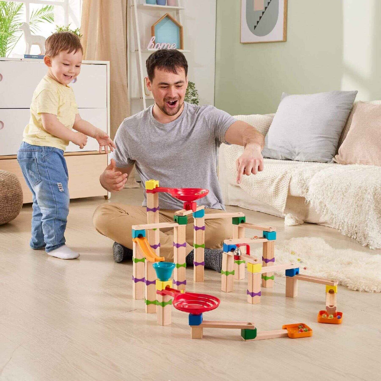 Man and child playing with Hape Tricks n Twists Marble Track in a living room.