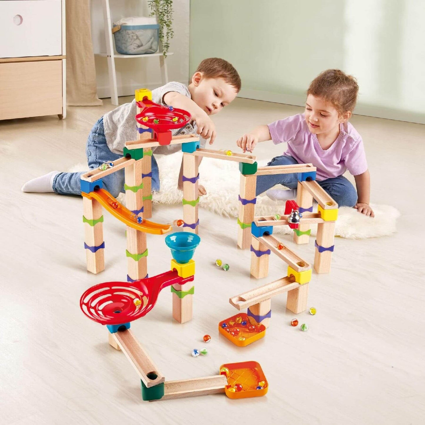 Two children playing with Hape Tricks n Twists Marble Track on a light-colored floor.