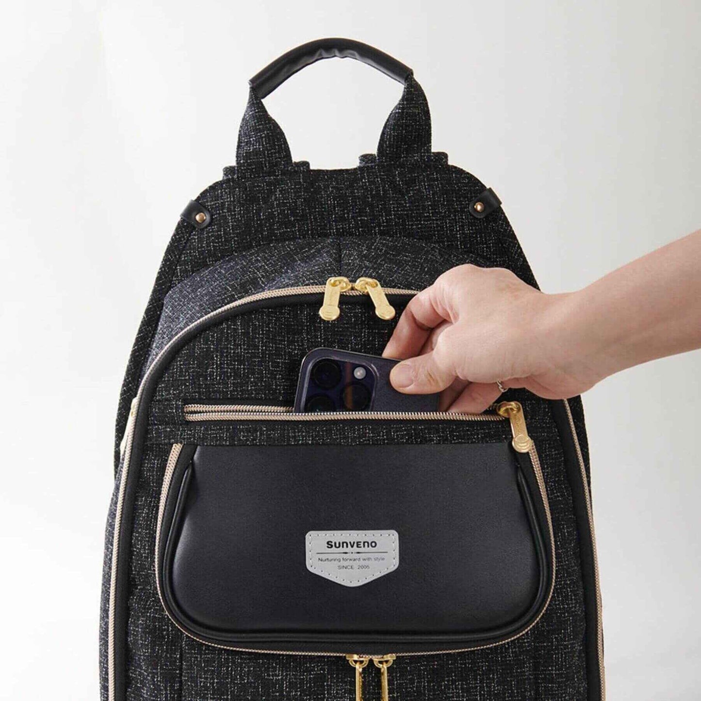 Sunveno Tweed Luxe Diaper Bag Backpack - Black and a hand placing a phone inside