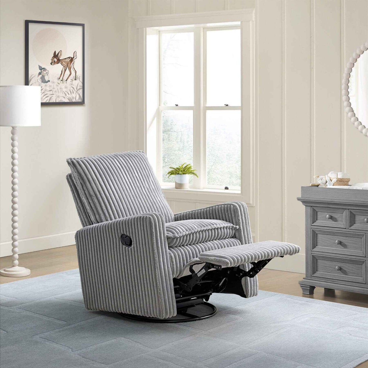 Uptown Nursery Swivel Rocker and Recliner in Corduroy Ash Gray in a living room setting with a lamp, plant, and dresser.