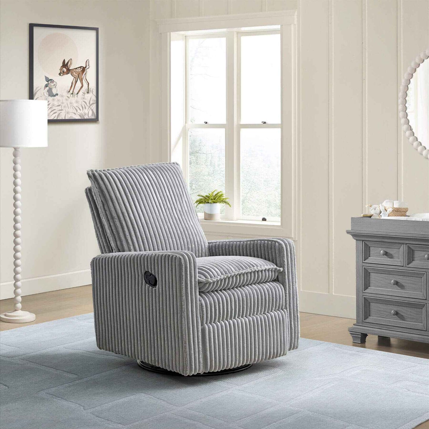 Uptown Nursery Swivel Rocker and Recliner in Corduroy Ash Gray in a living room setting with a lamp, window, and dresser.