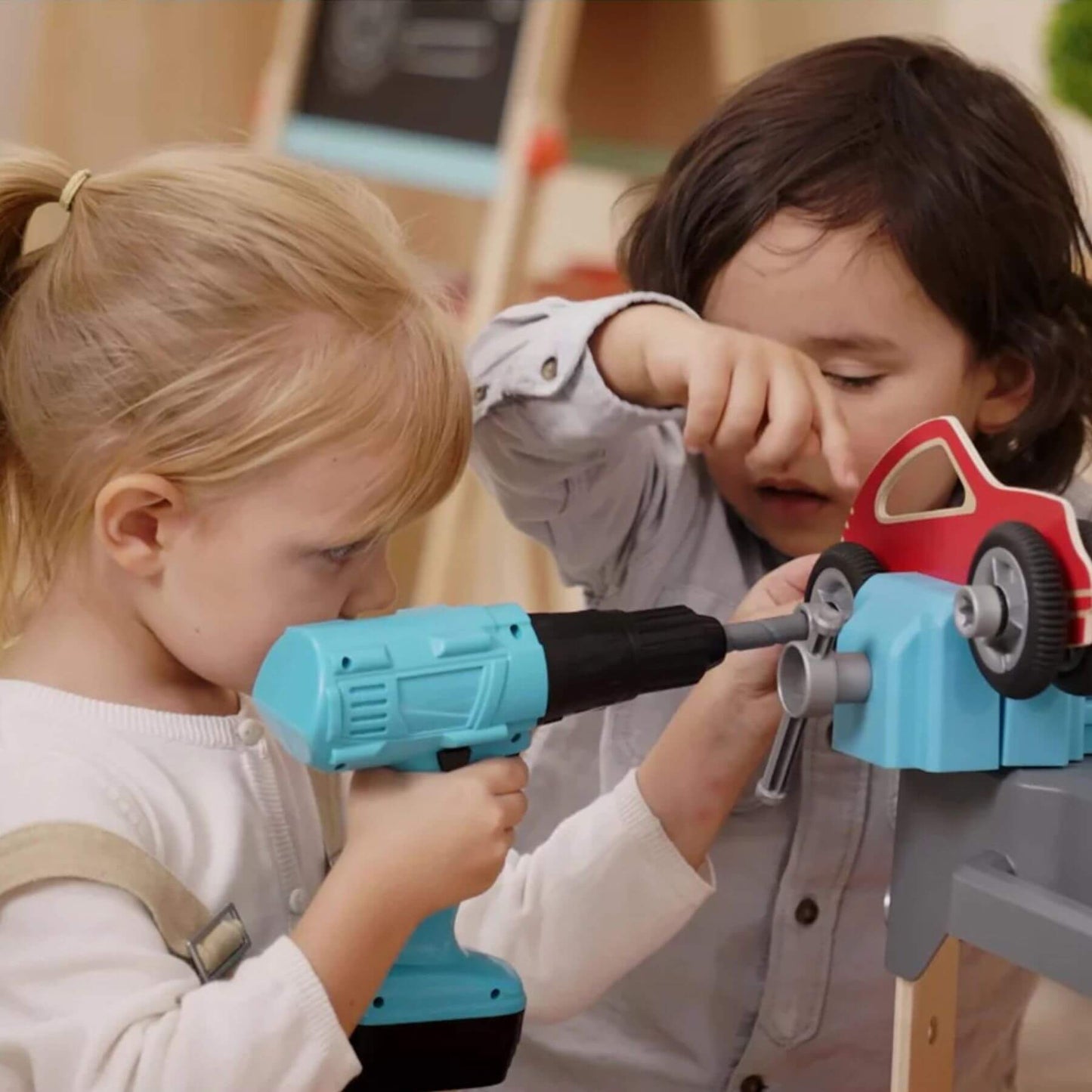 Two children playing with toy tools and a toy car.
