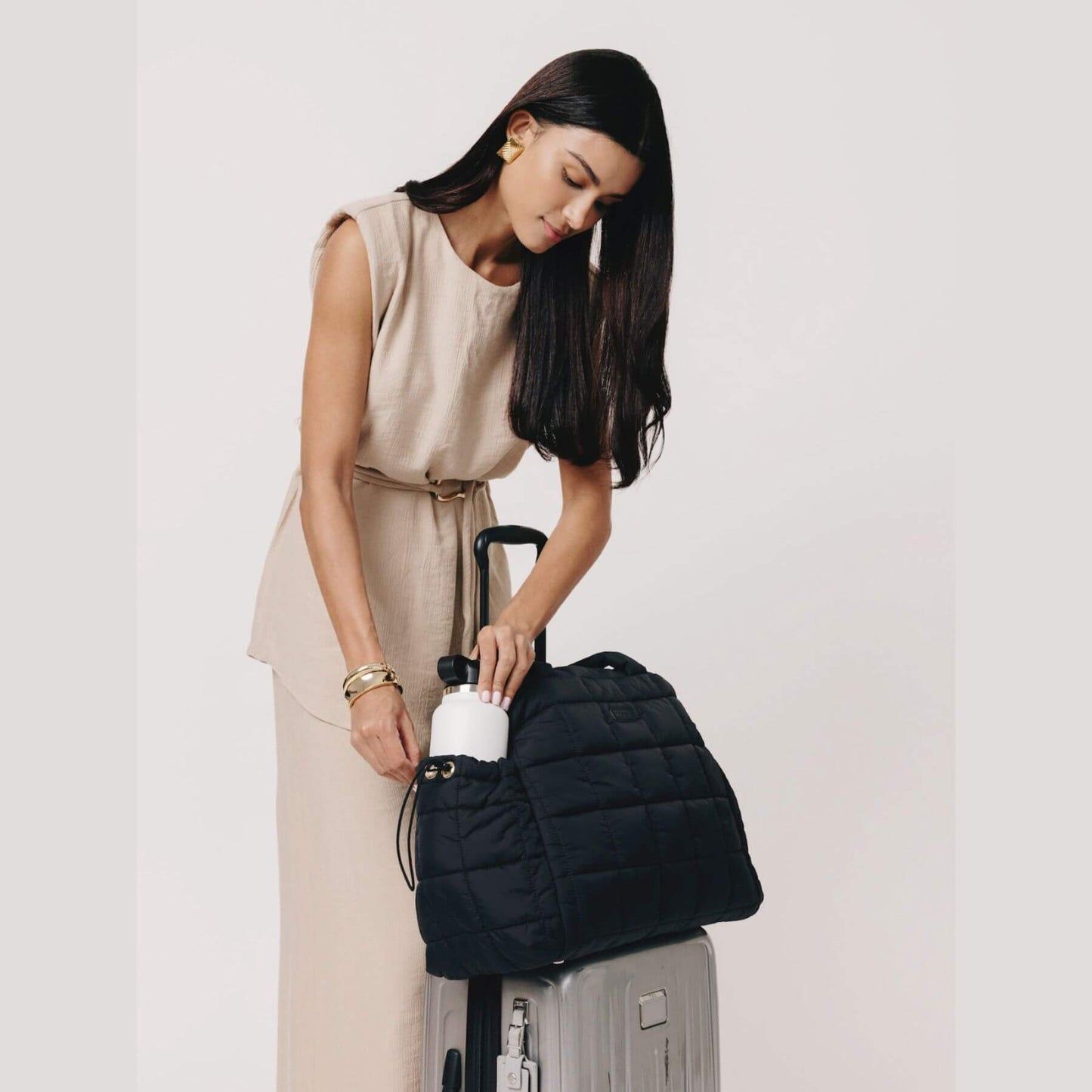 Woman holding augustnoa the weekender duffle bag black over a suitcase on a plain background