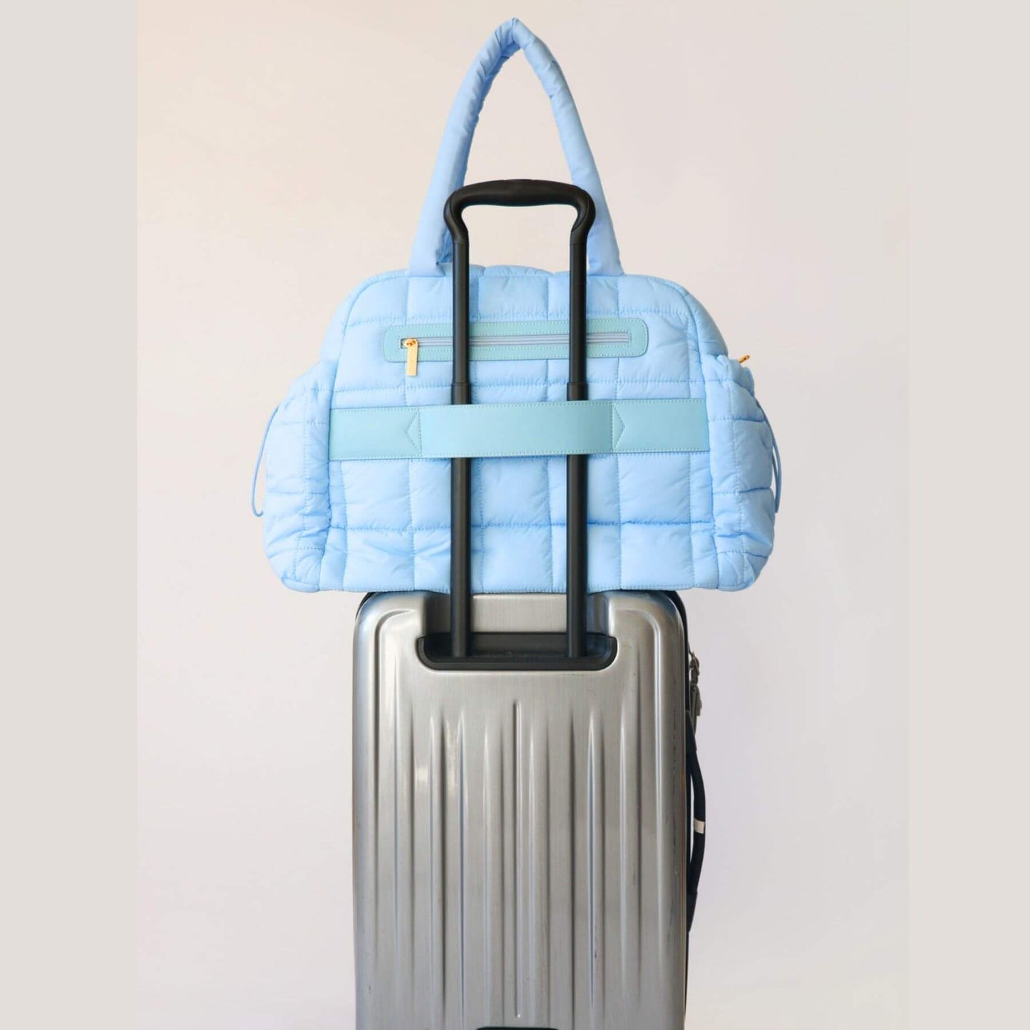 augustnoa the weekender duffle bag blue attached to a silver suitcase on a light gray background