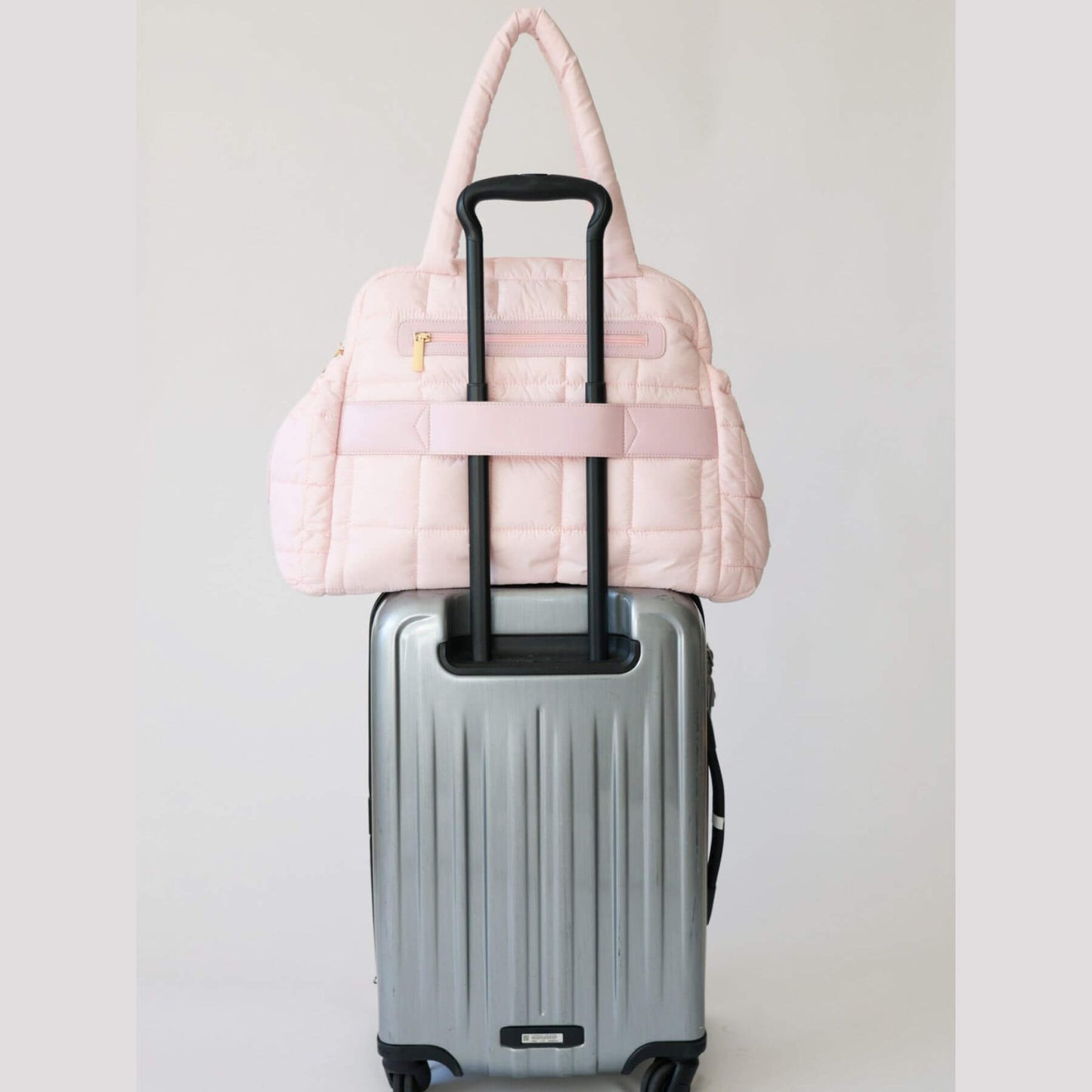 augustnoa the weekender duffle bag pink on top of a silver suitcase against a light gray background