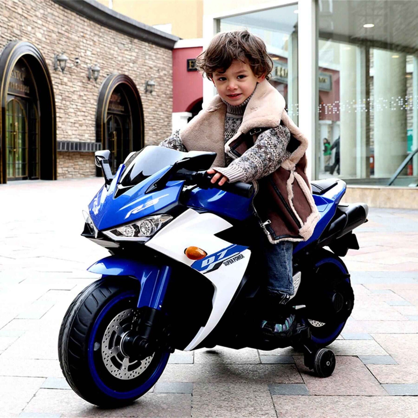 Child sitting on Tamco 12 V Kids Toys Electric Motorcycle with Training Wheels - Blue in an urban setting