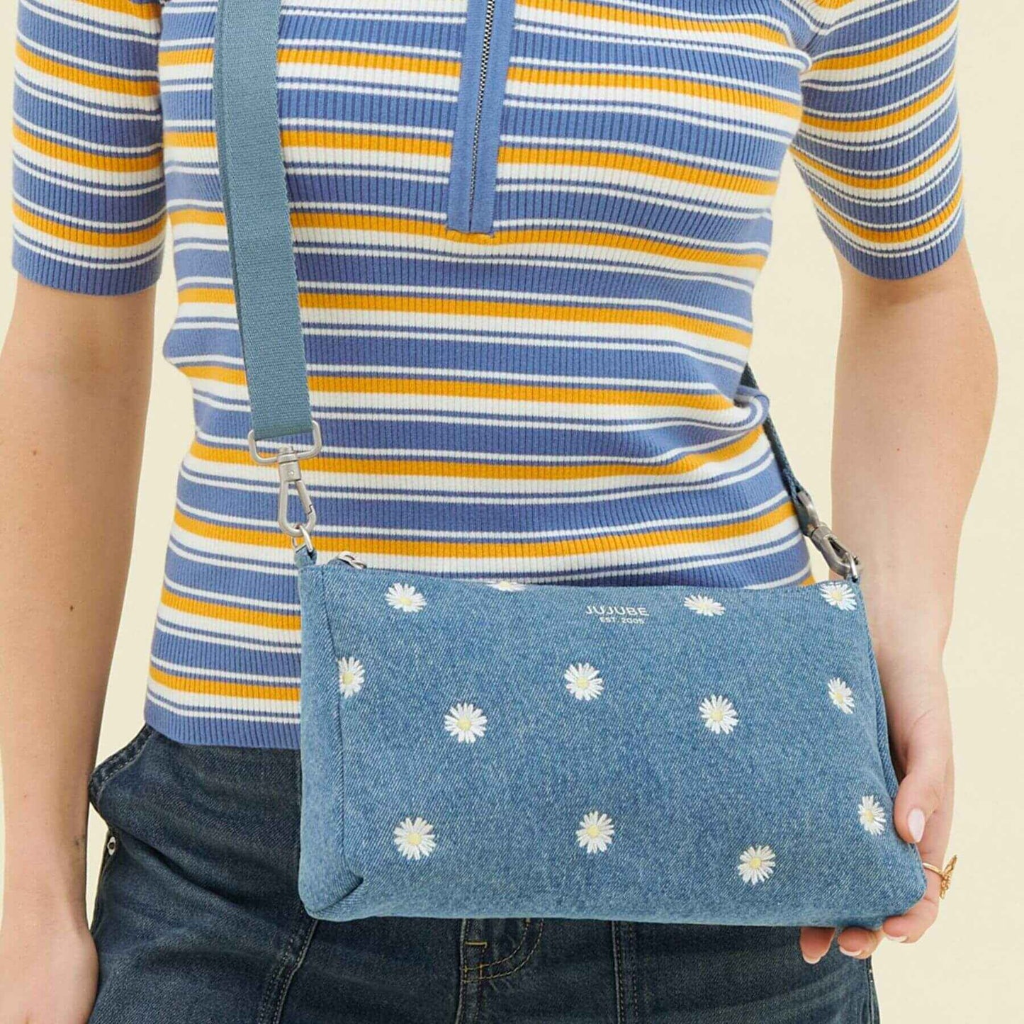 Person holding a blue denim bag with white floral patterns, wearing a striped shirt.