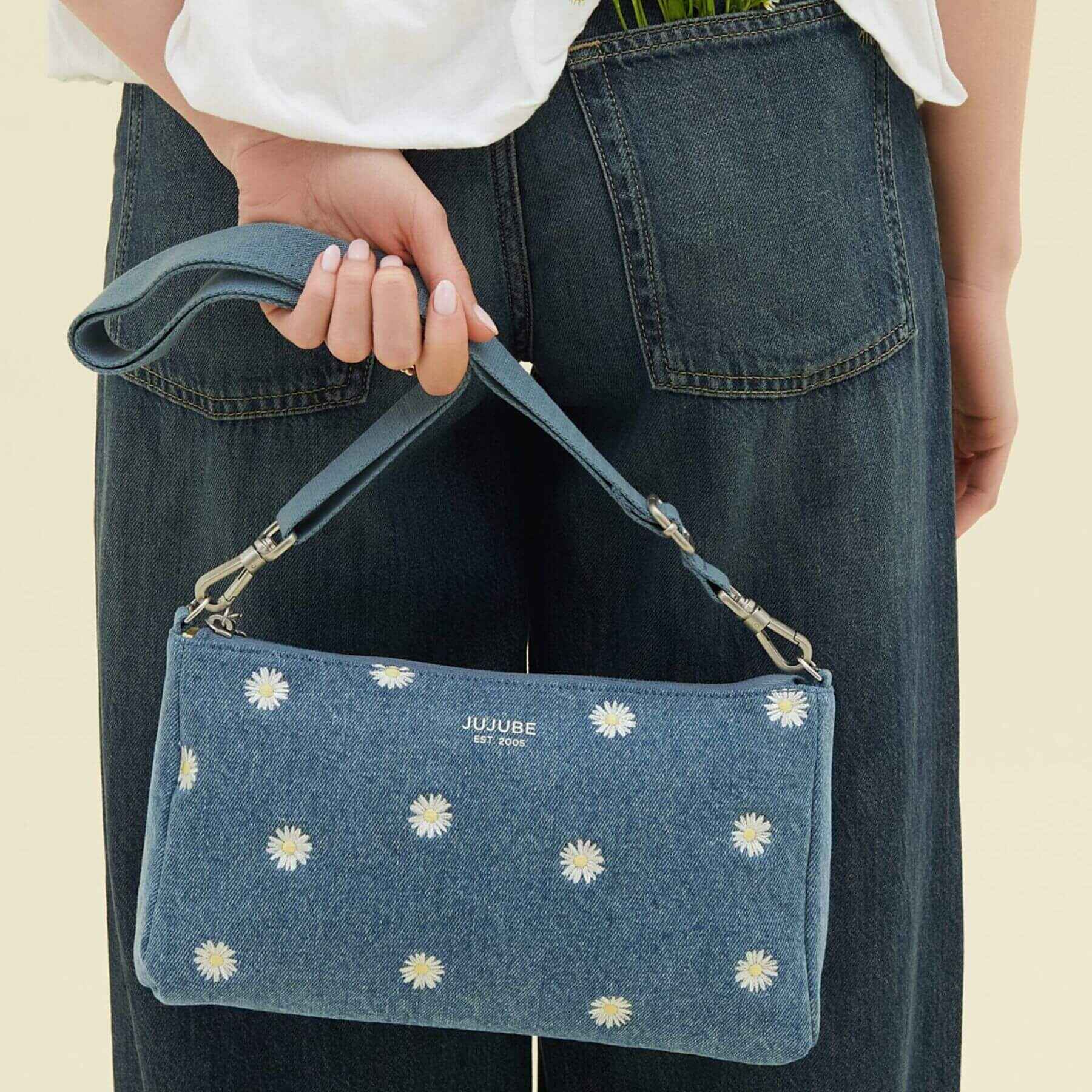 Blue denim handbag with white floral patterns held by a person wearing a white shirt and blue jeans.