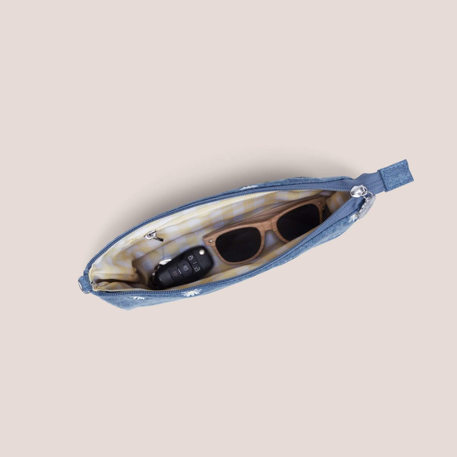 Blue pouch with sunglasses and phone inside on a beige background