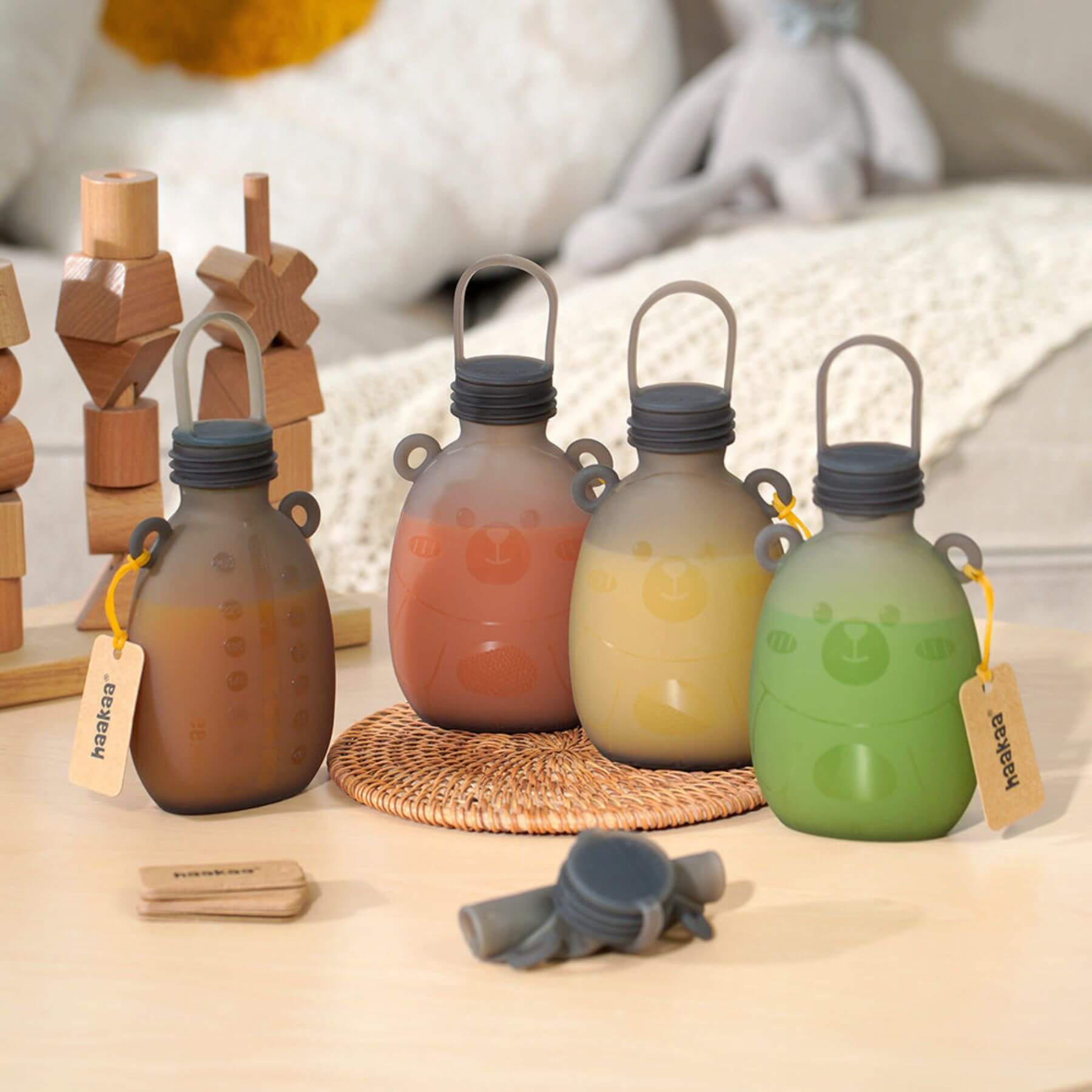 Set of Haakaa Happii Bear Silicone Goody Pouches with wooden stands on a neutral background