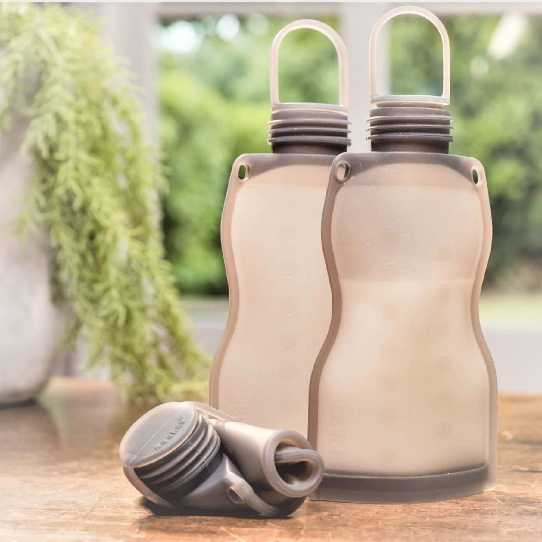 Two Haakaa Silicone Milk Storage Bag 9oz on a wooden surface outdoors.