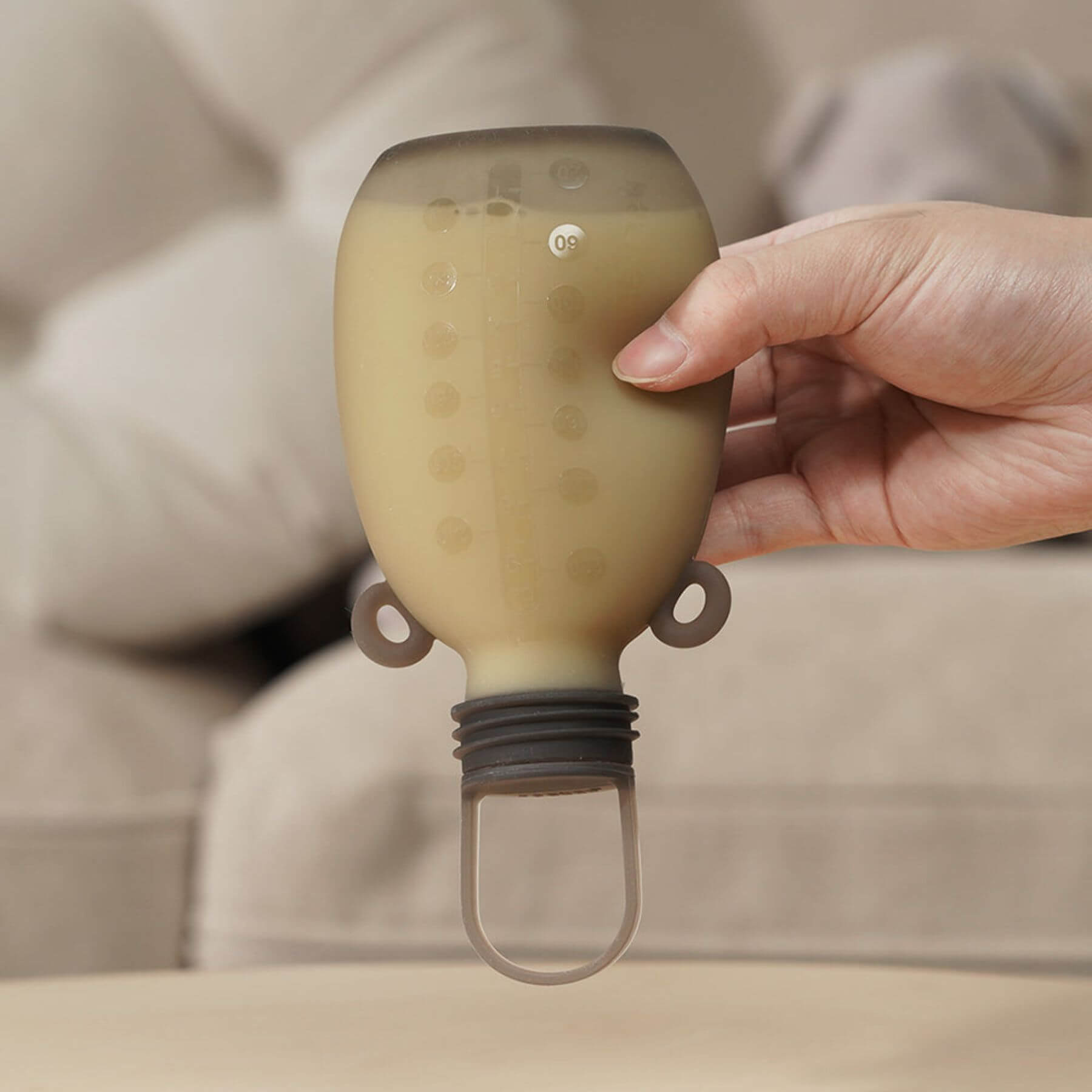 Hand holding a unique bottle-shaped object with a beige background