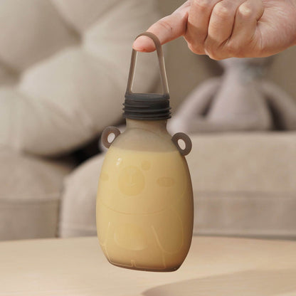 Hand holding a beige bottle with a handle against a blurred background