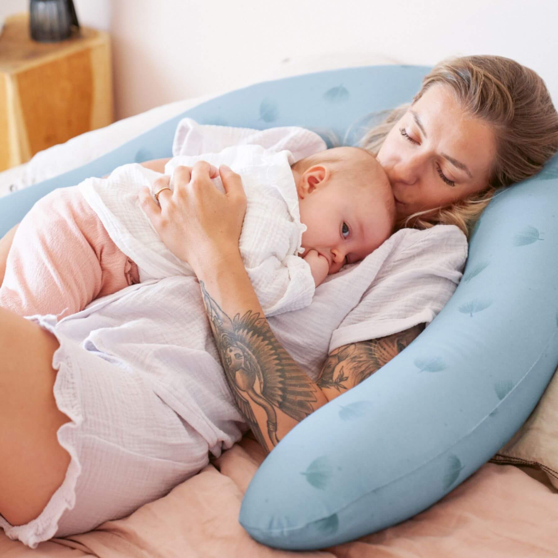 Woman holding a baby wrapped in a white blanket on B.Love U-Shape Pregnancy Pillow - Blue