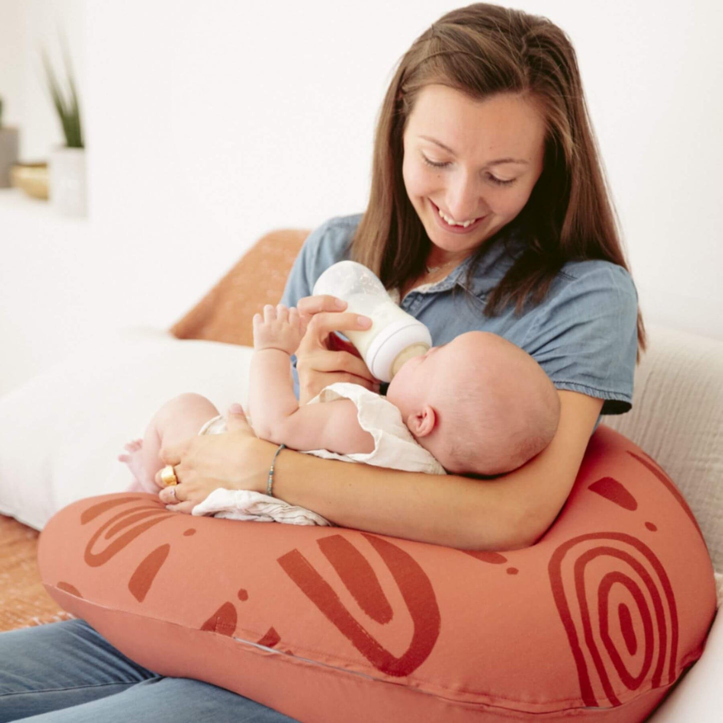 Woman holding a baby while sitting on a B.Love U-Shape Pregnancy Pillow - Terracotta