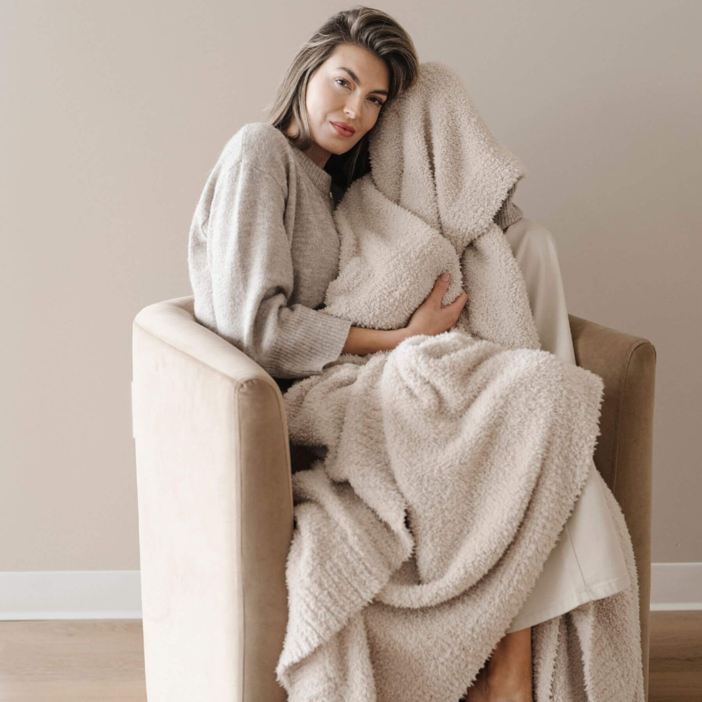 Woman sitting on a chair wrapped in BAMBONI® XL Blanket - Buttermilk in a cozy room.