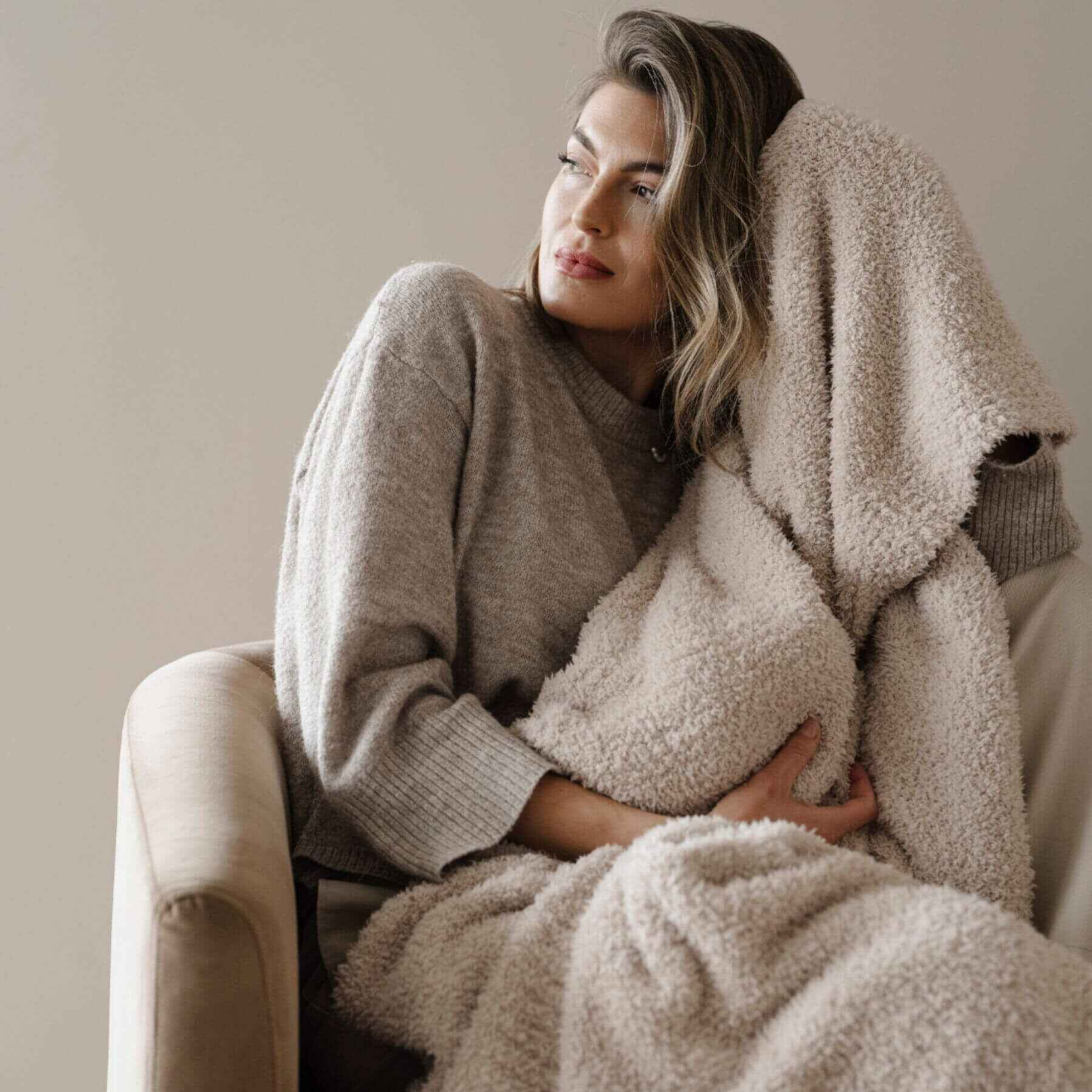 Woman wrapped in BAMBONI® XL Blanket - Buttermilk sitting on a couch against a neutral background