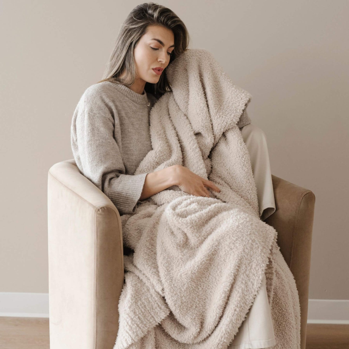 Woman sitting on a chair wrapped in BAMBONI® XL Blanket - Buttermilk in a cozy room.