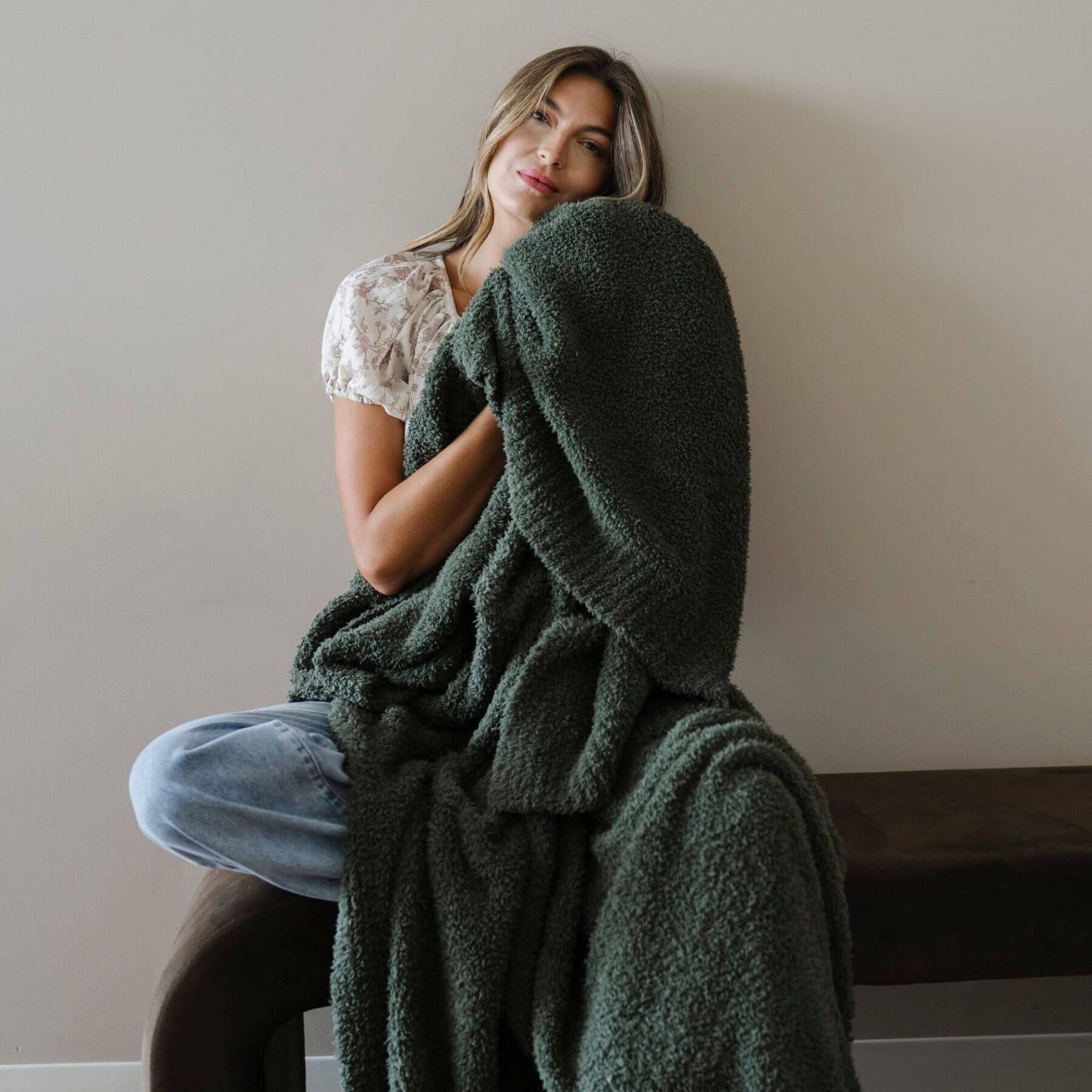 Woman wrapped in BAMBONI® XL Blanket sitting on a couch against a plain wall.