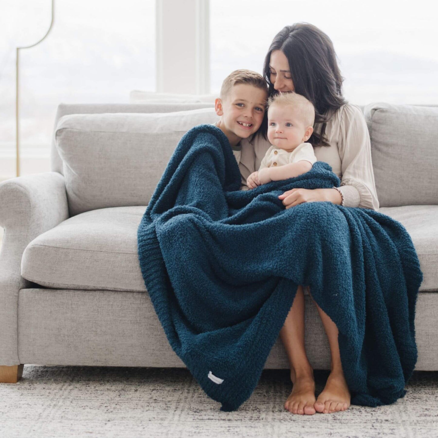 Woman and two children sitting on a couch under BAMBONI® XL Blanket - Nautical in a bright room.