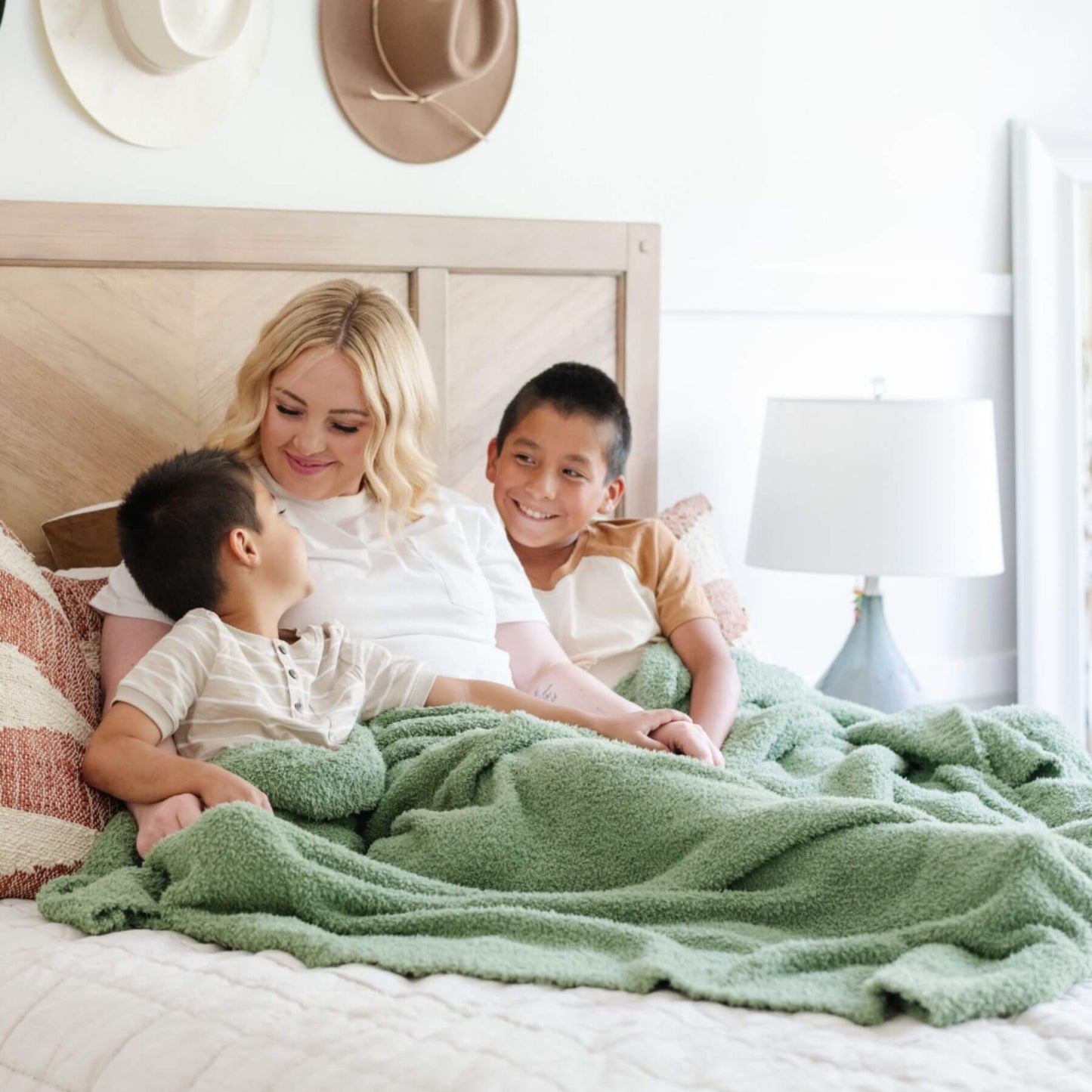 Woman and two children sitting on a bed with BAMBONI® XL Blanket - Olive