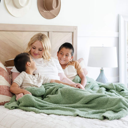 Woman and two children sitting on a bed with BAMBONI® XL Blanket - Olive