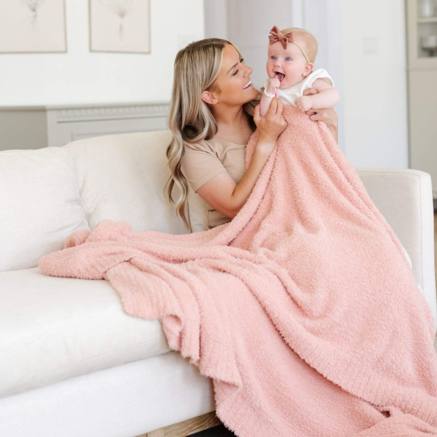 Woman holding a baby wrapped in BAMBONI® XL Blanket - Peach in a living room setting