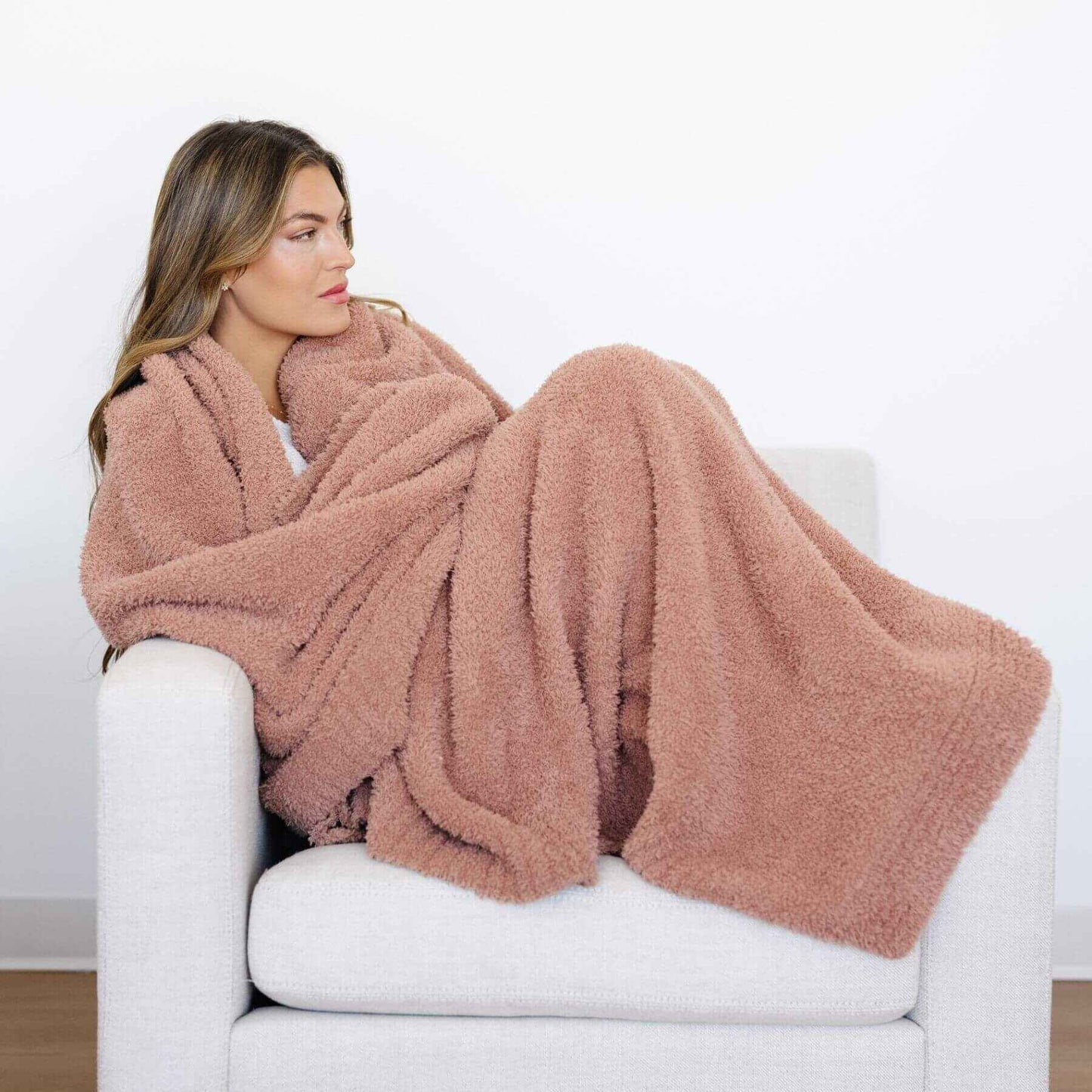 Woman wrapped in BAMBONI® XL Blanket - French Rose sitting on a white couch against a white background