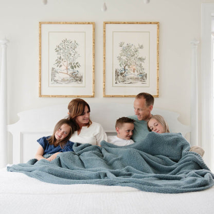 Family of five snuggling under BAMBONI® XL Blanket - Spruce on a bed with framed artwork on the wall.