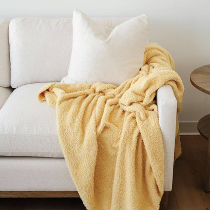 BAMBONI® XL Blanket - Sunburst draped over a white sofa with a wooden side table in the background.
