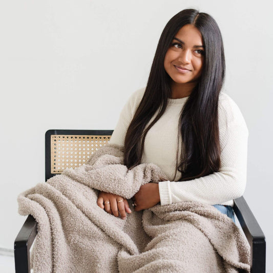 Woman sitting on a chair with BAMBONI® XL Blanket draped over her, wearing a white sweater.