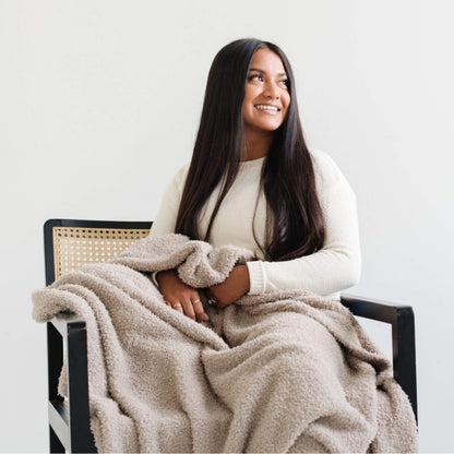 Woman sitting in a chair with BAMBONI® XL Blanket wrapped around her, smiling.