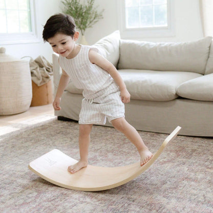 Child playing on a wooden balance board in a living room.