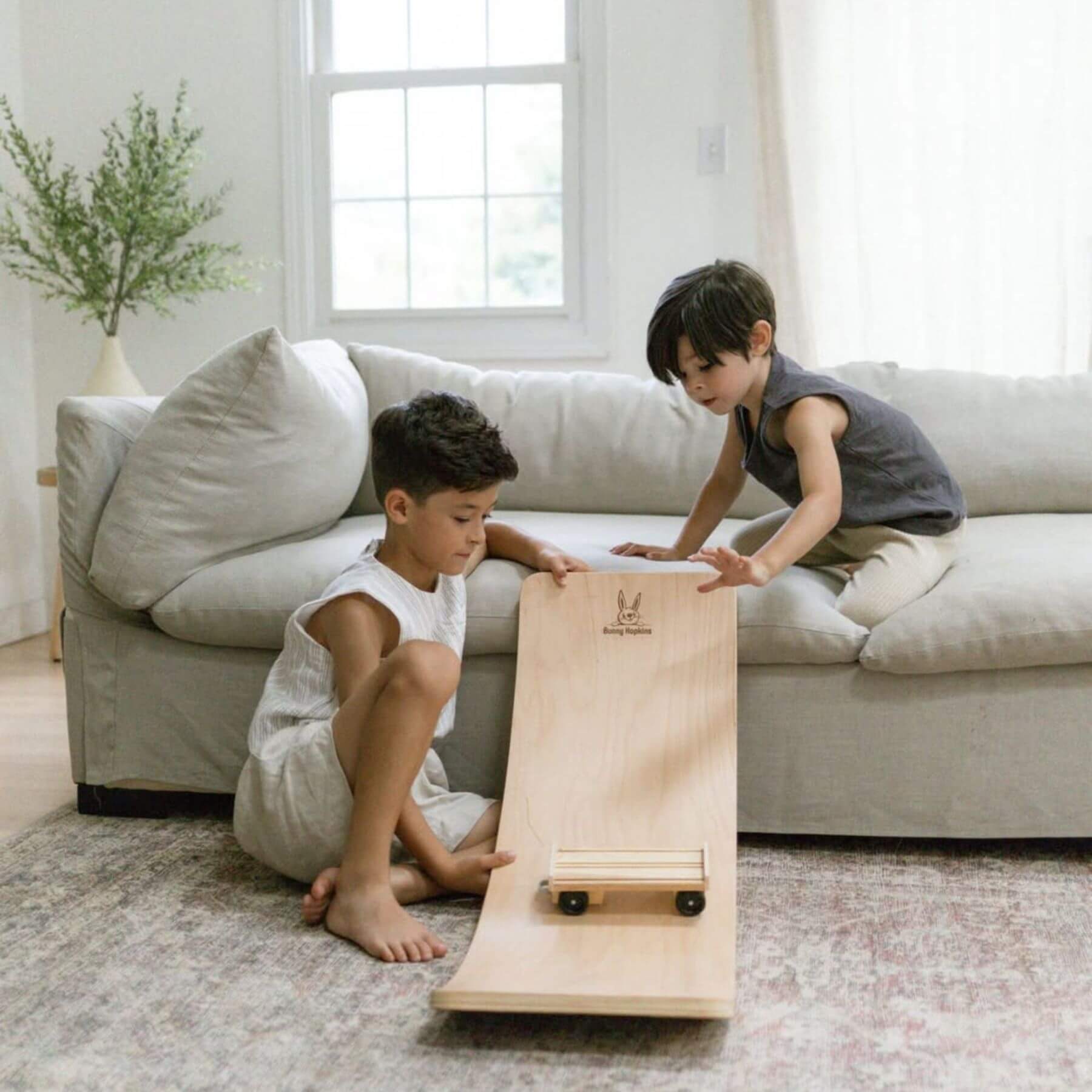 Two children playing with a wooden toy on a rug in a living room.