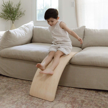 Child playing on a wooden board in a living room.