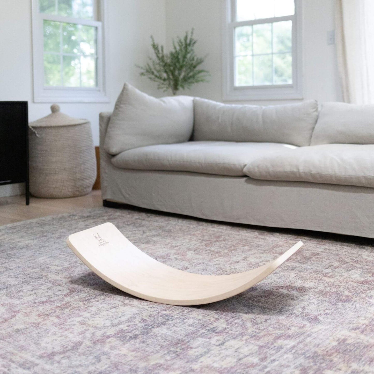 Light gray sofa in a living room with a curved wooden board on a patterned rug.