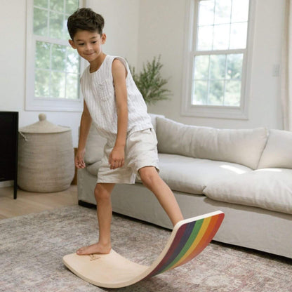 Child standing on a rainbow-colored balance board in a living room.