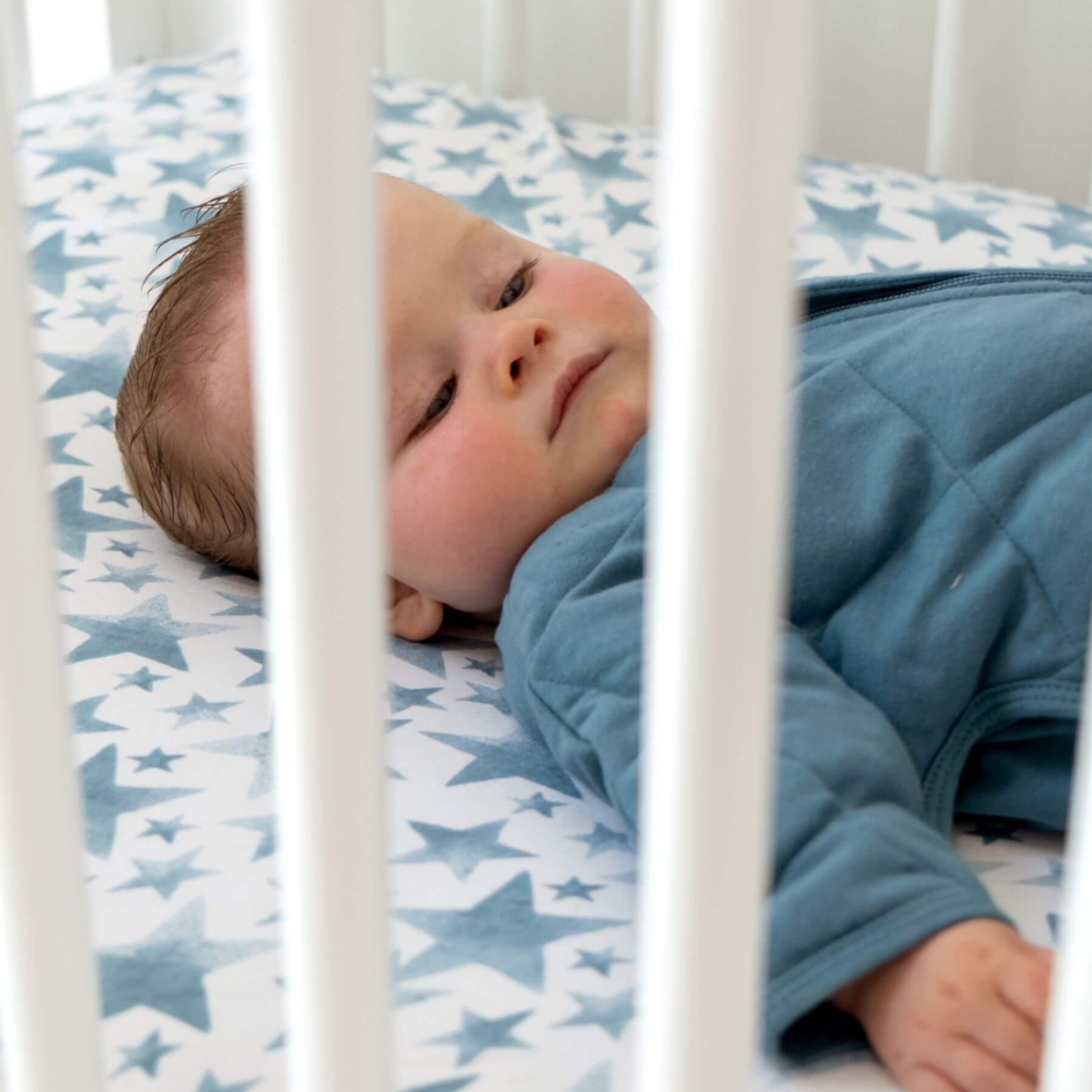Baby lying in a crib with blue and white star-patterned bedding