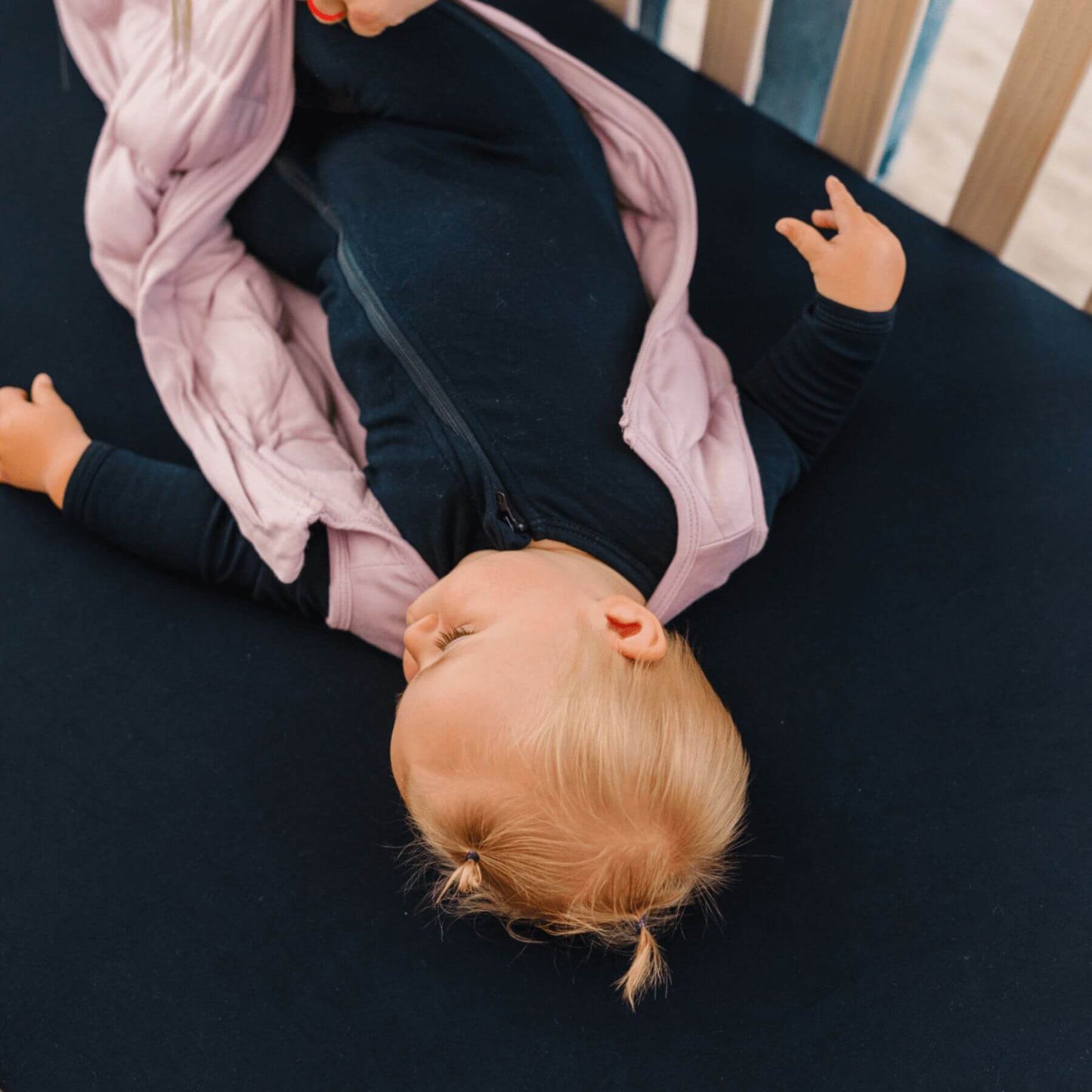 Baby lying on a black crib sheet with a pink swaddle