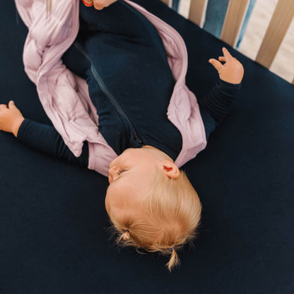 Baby lying on a black crib sheet with a pink swaddle